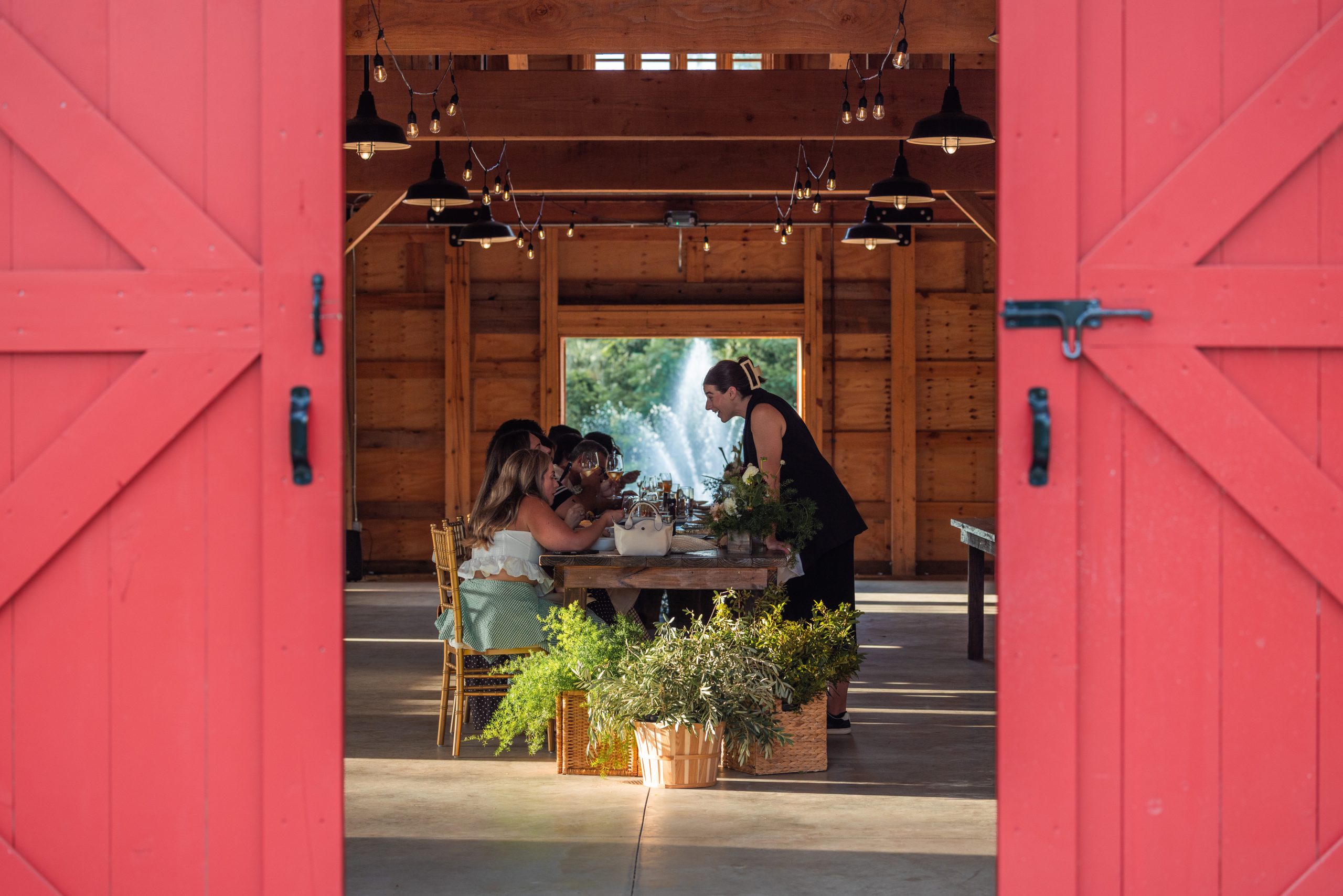 Guests share a seasonal meal inside the Red Barn at 4Roots Farm, surrounded by greenery and warm wood.